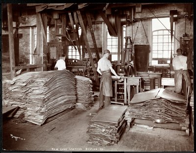Interior view of three men working with leather and heavy equipment at the New York Leather Belting Co., New York by Byron Company